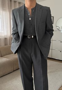 Costume gris sur mesure avec une chemise gris foncé texturée ; comprend une fermeture à boutons à l'avant et une ceinture noire avec une boucle argentée. Fond doux.