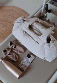 Beige quiltet taske med snøring, parret med bløde beige støvletter, metalvandflaske og mønstret telefonskal på en neutral overflade.