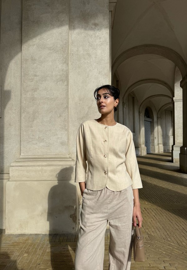 Beige button-up top with three-quarter sleeves, paired with light beige wide-leg pants. Structured design and subtle texture details.