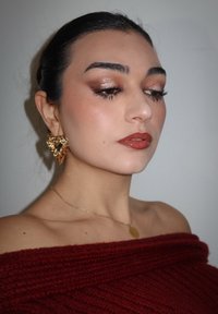 Modellen har på seg en burgunder off-shoulder topp, gullhjerteformede øredobber og et delikat gullkjede. Sminken har bronsefarger og glansfulle lepper.