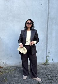 Brown leather blazer over a light cream sweater, dark wide-leg trousers, holding a pale yellow bag, and wearing black sunglasses.