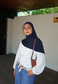 Langärmliges weißes Oberteil mit marineblauen Akzenten, Jeans, gemusterter Gürtel, kleine braune Umhängetasche und ein marineblauer Hijab.
