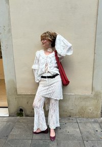 Fehér csipke blúz harangujjakkal, egy szintén csipkéből készült szoknya és nadrág felett. Piros kézitáskával és bordó cipőkkel kiegészítve.