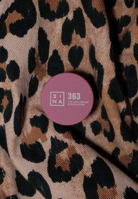 Rosa rund beholder merket "363 THE 24H CREAM EYESHADOW," plassert på et teksturert stoff med et beige og svart leopardmønster.