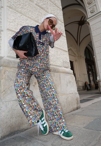 Conjunto de flores en diversos colores, con un cuello azul marino y acentos negros. Zapatillas verde y blanca completan el look, en un entorno de arquitectura de piedra.