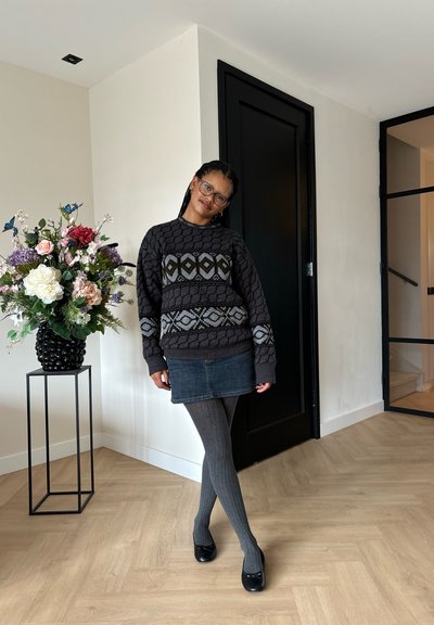 Suéter gris con un diseño geométrico, falda mini de mezclilla, medias gris de canalé y zapatos negros. Arreglo floral en un jarrón negro cercano.