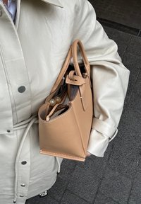 Brun skinnveske med en strukturert form, topphåndtak og en knyttet detalj. Glidelås-lukking, synlige sømmer og en glatt tekstur.