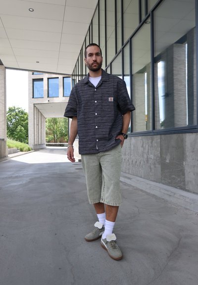 Camisa de manga corta abotonada en gris oscuro con un patrón horizontal; pantalones cortos hasta la rodilla de color verde claro; zapatillas grises con detalles en blanco.