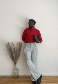 Outfit casual con un maglione a collo alto rosso e pantaloni a gamba larga grigio chiaro. Gli accessori includono una pochette verde e scarpe nere. Decorazione con erba pampas essiccata in un vaso di vetro.