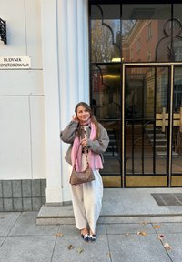 Grigia giacca oversize, sciarpa rosa, borsa a fantasia, pantaloni bianchi e scarpe a punta con design in bianco e nero, sullo sfondo di un edificio.