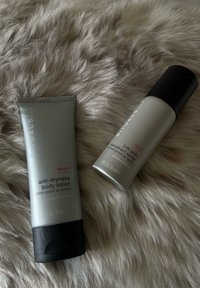 Dwa srebrnoszare produkty Rituals sport: balsam do ciała przeciw suchości oraz 24-godzinny spray antyperspiracyjny, umieszczone na miękkim beżowym futrze.