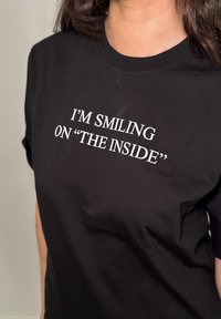 Black cotton t-shirt with white text that says "I'M SMILING ON 'THE INSIDE'" displayed on the front, featuring a crew neck design.
