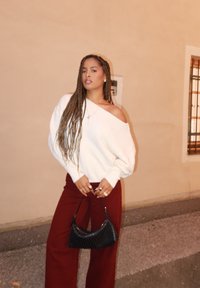 Witte oversized trui met doorgezakte schouders, gecombineerd met hooggetailleerde wijde benen broek in bordeauxrood. Zwarte geweven handtas en ringen als accessoires.