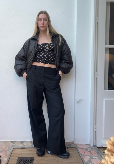 Chaqueta bomber negra, top corto de patrones con lunas crecientes, pantalones de pierna ancha negros a medida y zapatillas chunky negras. Superficie texturizada.