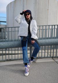 Quilted white jacket over a gray hoodie, paired with patchwork blue denim jeans and colorful sneakers with laces and a patterned design.