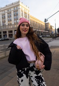 Doudoune noire superposée sur un sweat-shirt rose clair, associée à un pantalon à motifs noir et blanc. Tenant un petit sac à main rose.