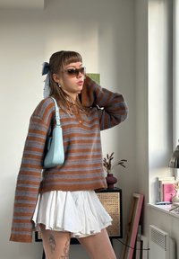 Stribet brun og blå sweater, tilpasset ved taljen. Hvid plisseret nederdel, lyseblå håndtaske. Tilbehør inkluderer solbriller og hårbånd.