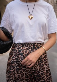 T-shirt en coton blanc associé à une jupe à imprimé léopard. Les accessoires comprennent un pendentif en cœur doré, un bracelet doré et un sac tissé noir.