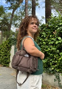 Brun totebag med fleece-textur, med robuste håndtak og en logo. Båret casual mot en bakgrunn av grønt.