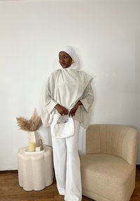 Bluză supradimensionată din cremă mătăsoasă, pantaloni albi cu picior larg și o geantă albă texturată. Scaun sculptural bej și vază decorativă în fundal.