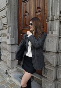 Szürke kockás blézer krémszínű garbóval, fekete miniszoknyával kombinálva. Kiegészítők: fekete napszemüveg és fekete táska.