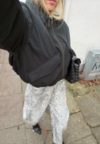 Sort dunjakke med lynlås og to forlommer, kombineret med højtaljede hvide bukser med slangeprint og sorte ankelstøvler med spids snude.