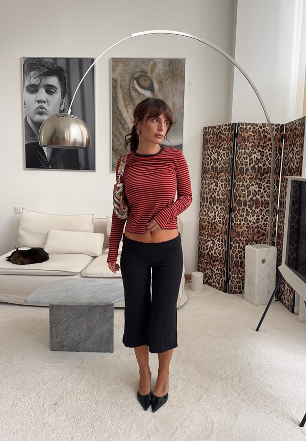 Mujer con top de rayas rojas y negras y culottes negros de pie en una sala de estar moderna con pantalla de estampado de leopardo y gran arte de pared.