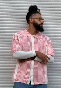 Camisa de manga curta com padrão vermelho e branco e gola, tecido texturizado, camada interior de manga comprida branca e jeans azuis.