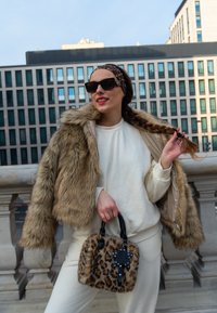 Kailas mākslīgās kažokādas jakas īsā versija, brūnā krāsā, virs baltā krekla ar garām piedurknēm. Beigē uz leopardu līdzīgā raksta somiņa ar melnu rokturi un zvaigznes akcentu. Kvadrātveida saulesbrilles.