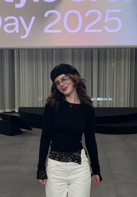 Top noir à manches longues avec détails en dentelle, pantalon blanc taille haute, et béret noir. Des lunettes transparentes apportent une touche moderne sur un fond neutre.