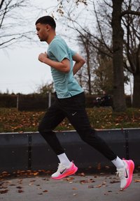 Chemise de sport bleu clair et pantalon de survêtement noir portés lors de la course. Chaussures Nike blanches et roses avec des accents noirs. Feuilles d'automne au sol.