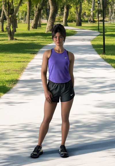 Joven en top morado y shorts negros de pie en un sendero del parque soleado y serpenteante, rodeada de árboles y hierba verde.