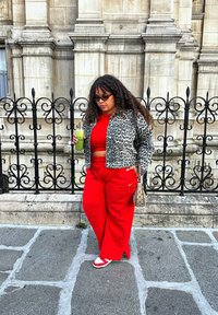 Red wide-leg trousers paired with a red crop top underneath a patterned grey leopard print jacket. Holding a green beverage, with a small bag and patterned trainers.