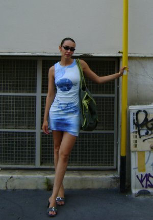 Vestido mini sin mangas en azul y blanco con un diseño gráfico circular. La tela es suave, y la modelo lleva puestas gafas de sol oscuras y sostiene un bolso verde.