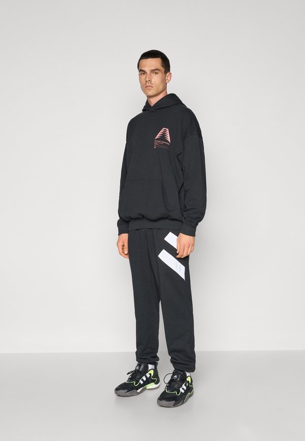 Svart hettegenser med en rosa grafikk, kombinert med svarte bukser med hvite diagonale striper. Svarte joggesko med grønne detaljer.