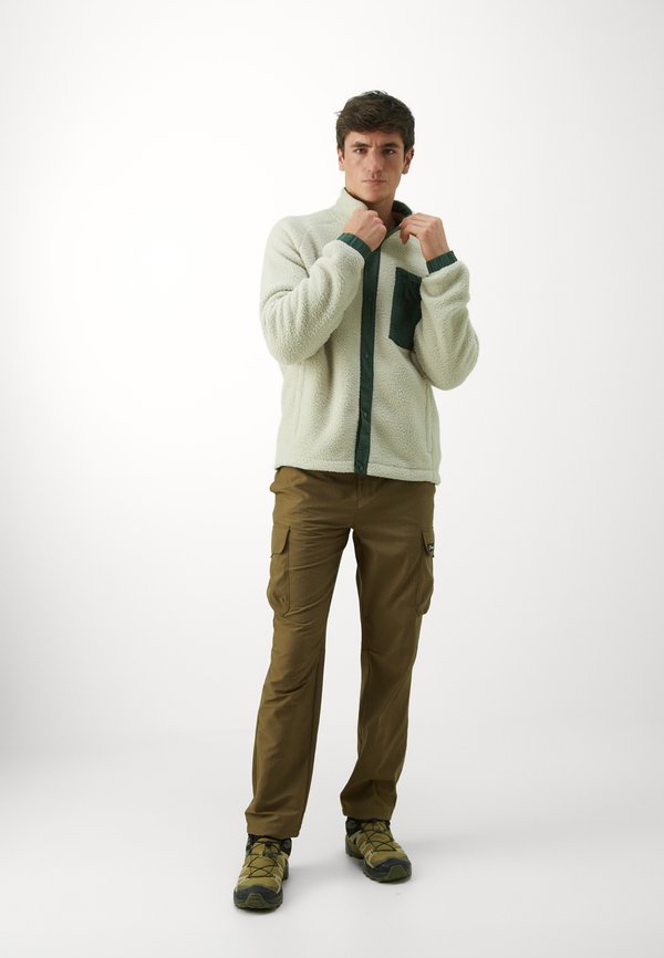 Kreminė flisinė striukė su tamsiai žaliais mygtukais ir kišene, derinama su rudomis kargo kelnėmis ir pilkomis lauko bateliais.