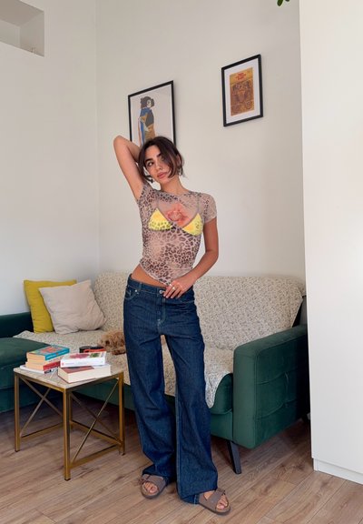 Top corto de estampado de leopardo transparente, combinado con un bikini amarillo, y unos pantalones vaqueros de campana de cintura alta en azul oscuro, junto con sandalias marrones.