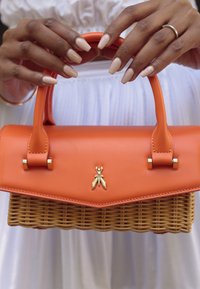 Orange Handtasche mit strukturiertem Design, ausgestattet mit einer glatten Lederoberfläche und einem geflochtenen Korbus. Goldene Bienenakzent an der Vorderseite.
