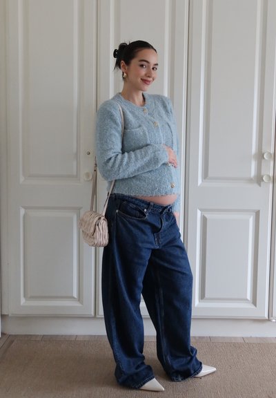 Cardigan texturizado azul claro con botones dorados, combinado con jeans oscuros holgados y zapatos blancos de punta. Pequeño bolso crema utilizado como bandolera.