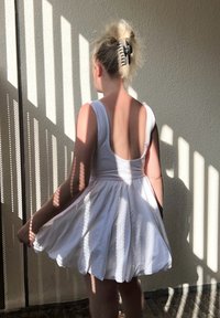 Robe blanche sans manches avec un corsage ajusté et une jupe évasée, présentant un dos plongeant. Le tissu semble lisse, avec la lumière du soleil créant des motifs d'ombre.