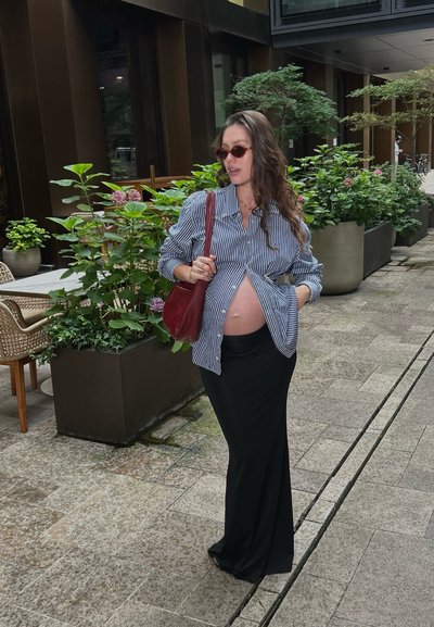 Camisa a rayas azul y blanca, abierta por el frente, combinada con una falda larga negra. Los accesorios incluyen gafas de sol rojas y un bolso burdeos.