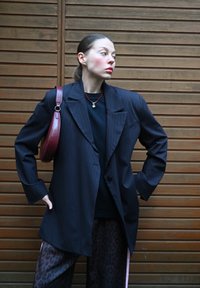 Blazer bleu marine à rayures, avec une coupe cintrée, assorti à une chemise noire et un pantalon à imprimé léopard. Accessoirisé avec un sac bourgogne et un collier.