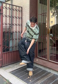 Polo às riscas verdes e brancas com colarinho, combinado com jeans escuros largos e botas de trabalho castanhas. Chaveiro notável preso aos jeans.