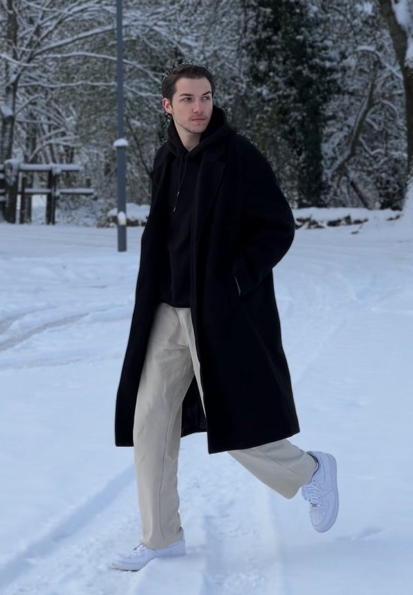 Juodas vilnonis paltas, juoda sweatshirt, rausvos kelnės ir baltos sportbačiai, dėvimi snieguotoje aplinkoje. Fone matyti medžiai ir snieguota žemė.