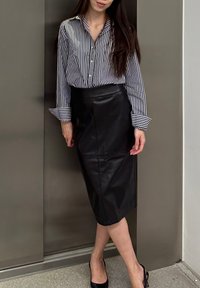 Chemise à rayures noir et blanc, associée à une jupe crayon en cuir noir élégante et des talons noirs. Design moderne et ajusté.