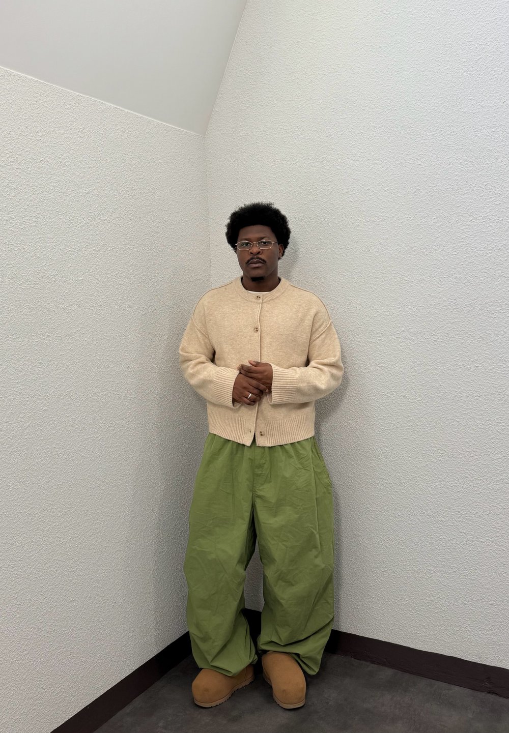 Cardigan en tricot beige avec un col rond et des boutons, associé à un pantalon vert ample. Des chaussons en daim marron complètent la tenue.