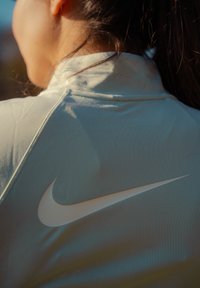 Közeli kép egy személyről, aki világoskék Nike dzsekit visel, a logó jól látható a háton természetes fényben.