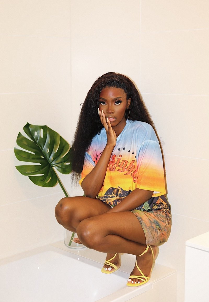 Oversized gradient t-shirt in shades of orange and blue, adorned with mountain graphics. Complemented by yellow strappy heels, set against a neutral background.