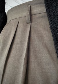 Jupe plissée gris charbon avec une taille ajustée, en tissu texturé, présentant des plis verticaux et des détails de couture subtils.