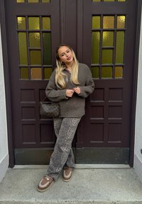 Καφέ oversized πλεχτό πουλόβερ, παντελόνι με λεοπάρ σχέδιο και καφέ πλατφόρμες. Τα αξεσουάρ περιλαμβάνουν μια τσάντα με σχέδιο. Το φόντο περιλαμβάνει καφέ πόρτες.